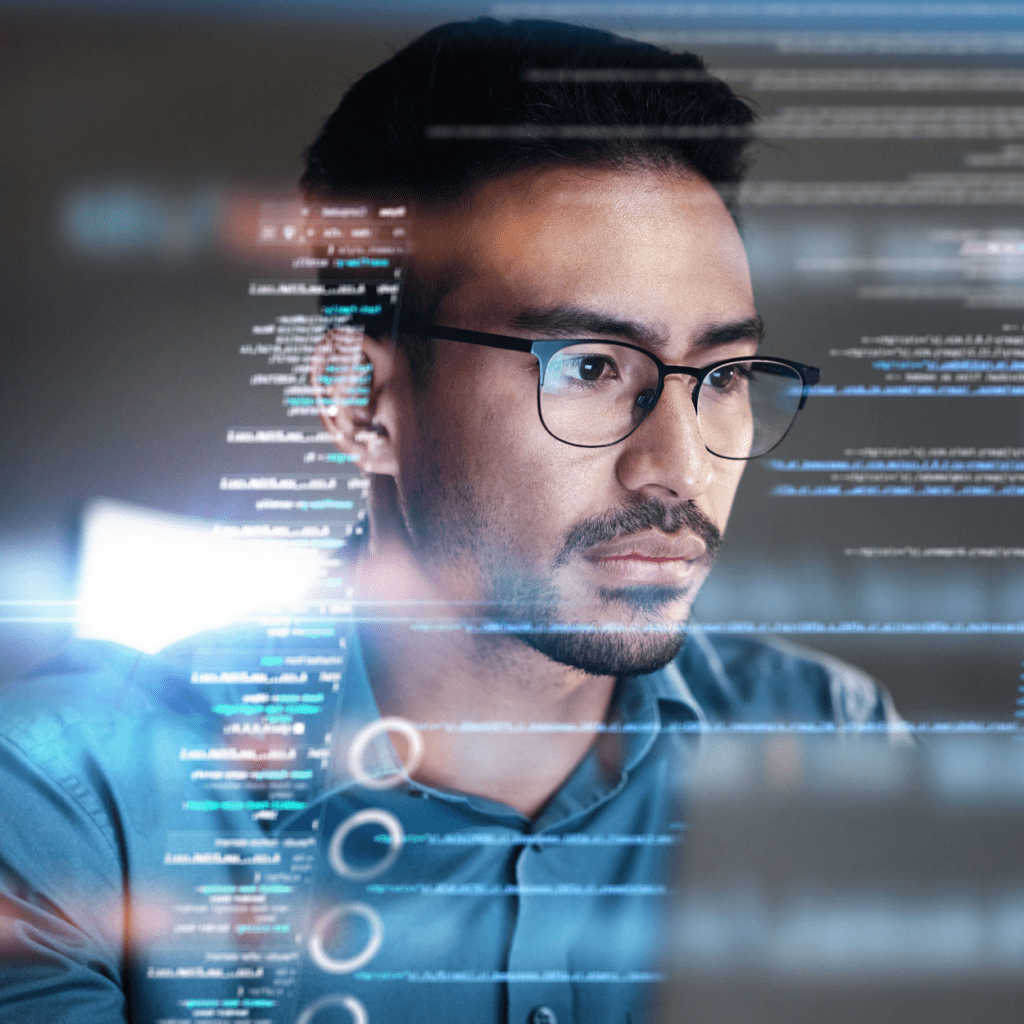 A man wearing glasses and a blue shirt is focusing intently on a computer screen displaying various lines of code and data. The image suggests a programming or software development environment with a futuristic, high-tech ambiance.